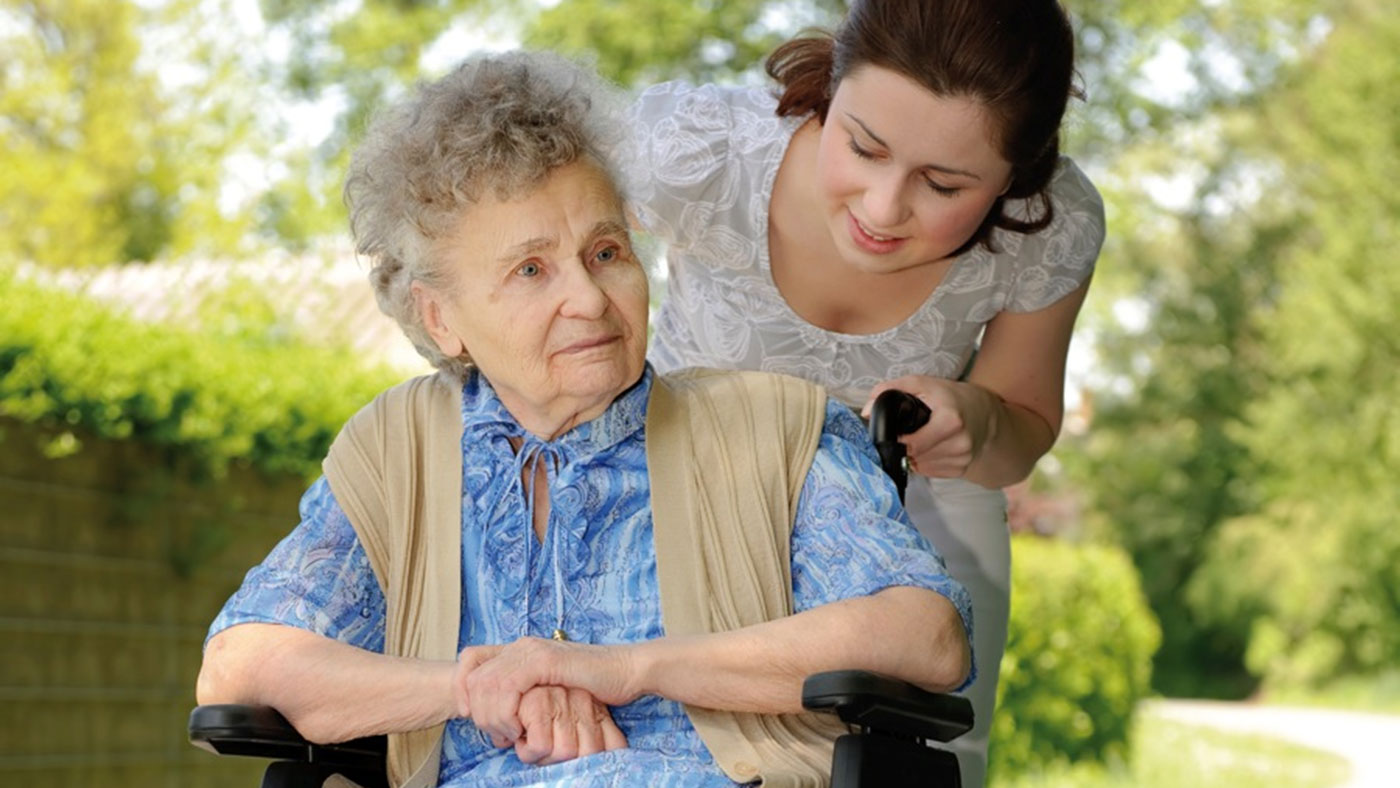 Junge Frau spaziert mit Seniorin im Rollstuhl