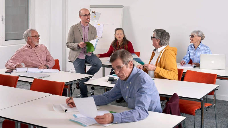 Seniorinnen und Senioren sitzen im Kursraum und blicken zum Kursleiter.