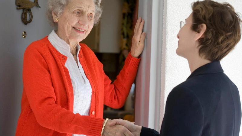 Ortsvertreterin begrüsst Seniorin an der Türe.