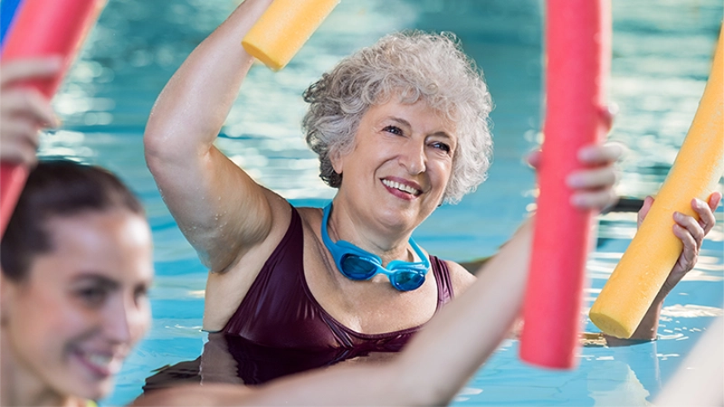 Eine Seniorin liegt beim Wasserfitness auf dem Rücken in Wasser und trainiert ihre Beine.