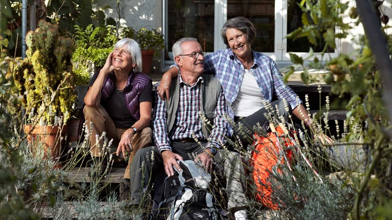 Drei Seniorinnen und Senioren machen beim Wandern eine Pause.