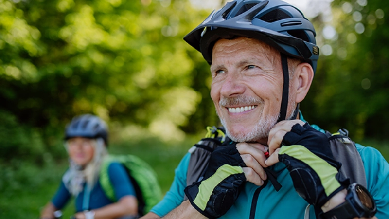 Eine ältere Frau und ein älterer Mann mit dem Velo unterwegs auf einem Waldweg.