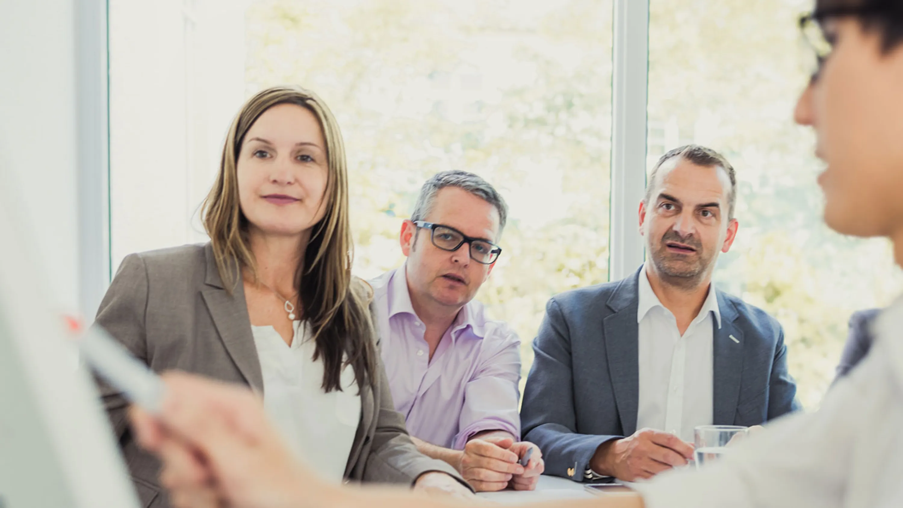 Eine Frau und zwei Männer blicken zu einem weiteren Mann, der eine Präsentation hält.