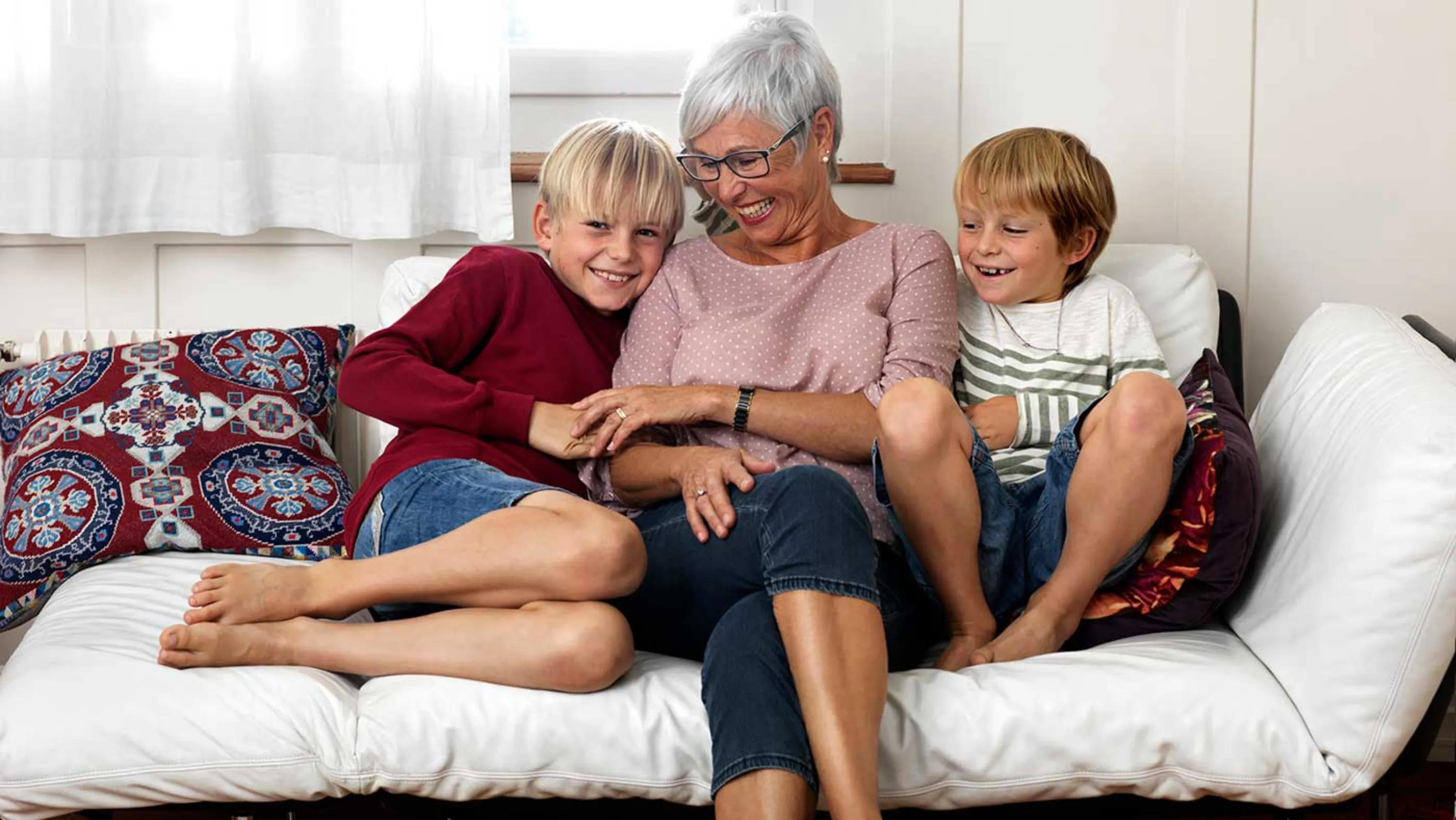 Grossmutter sitzt zusammen mit ihren zwei Enkeln glücklich auf dem Sofa.