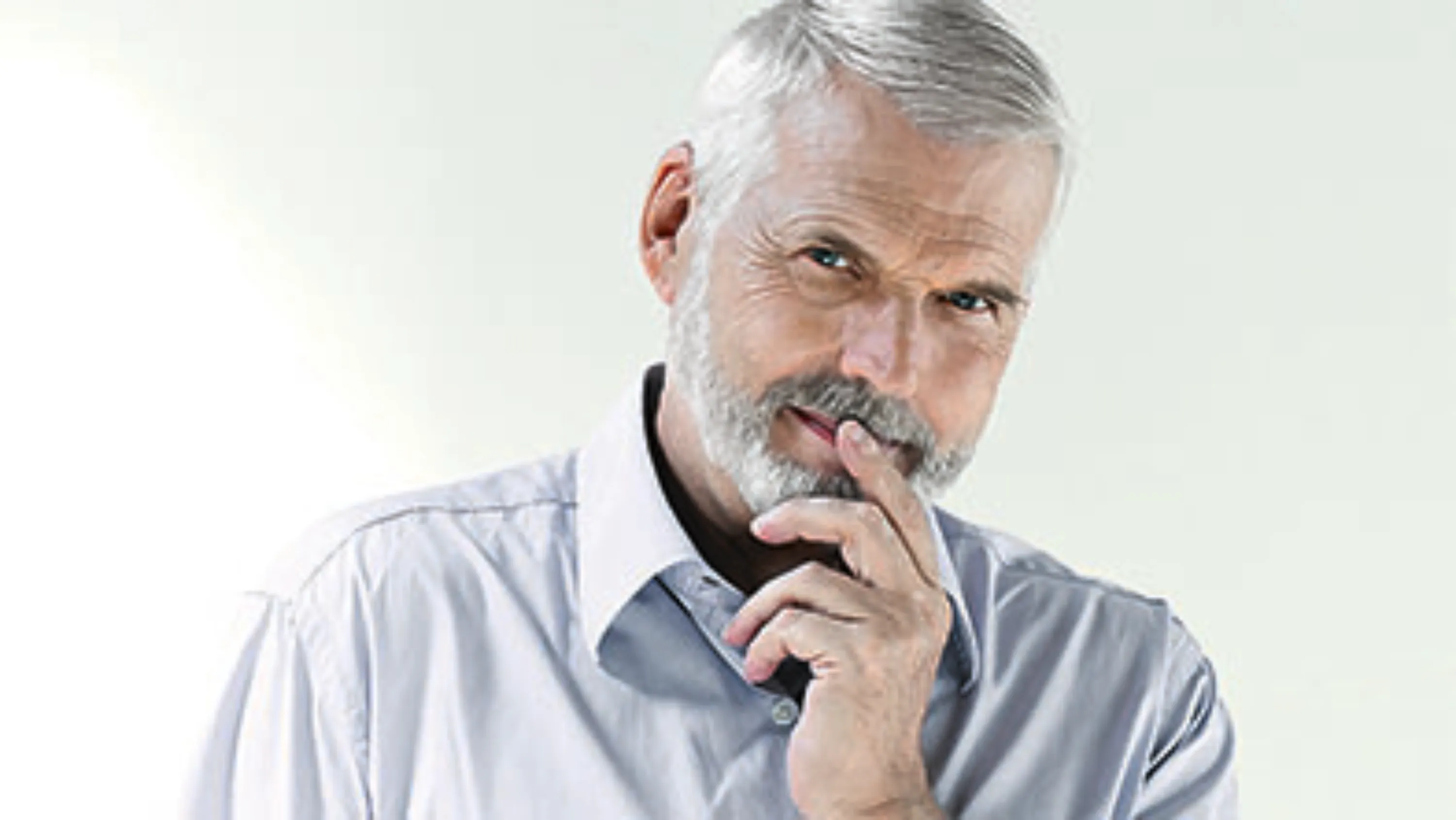 Mann mit grau melierten Haaren hält sich mit der Hand das Kinn und blickt in die Kamera.