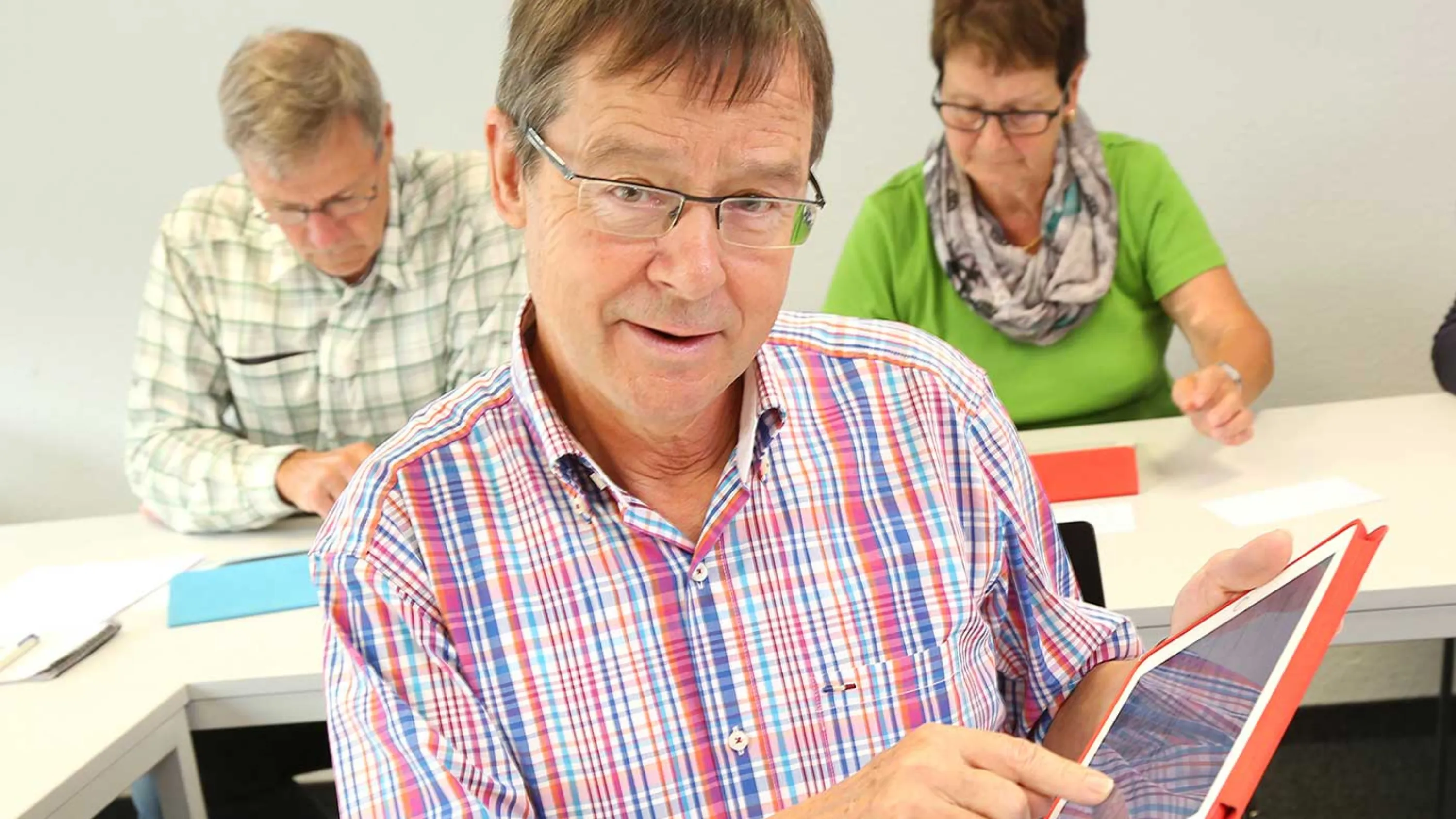Senior bedient das Tablet und blickt in die Kamera.