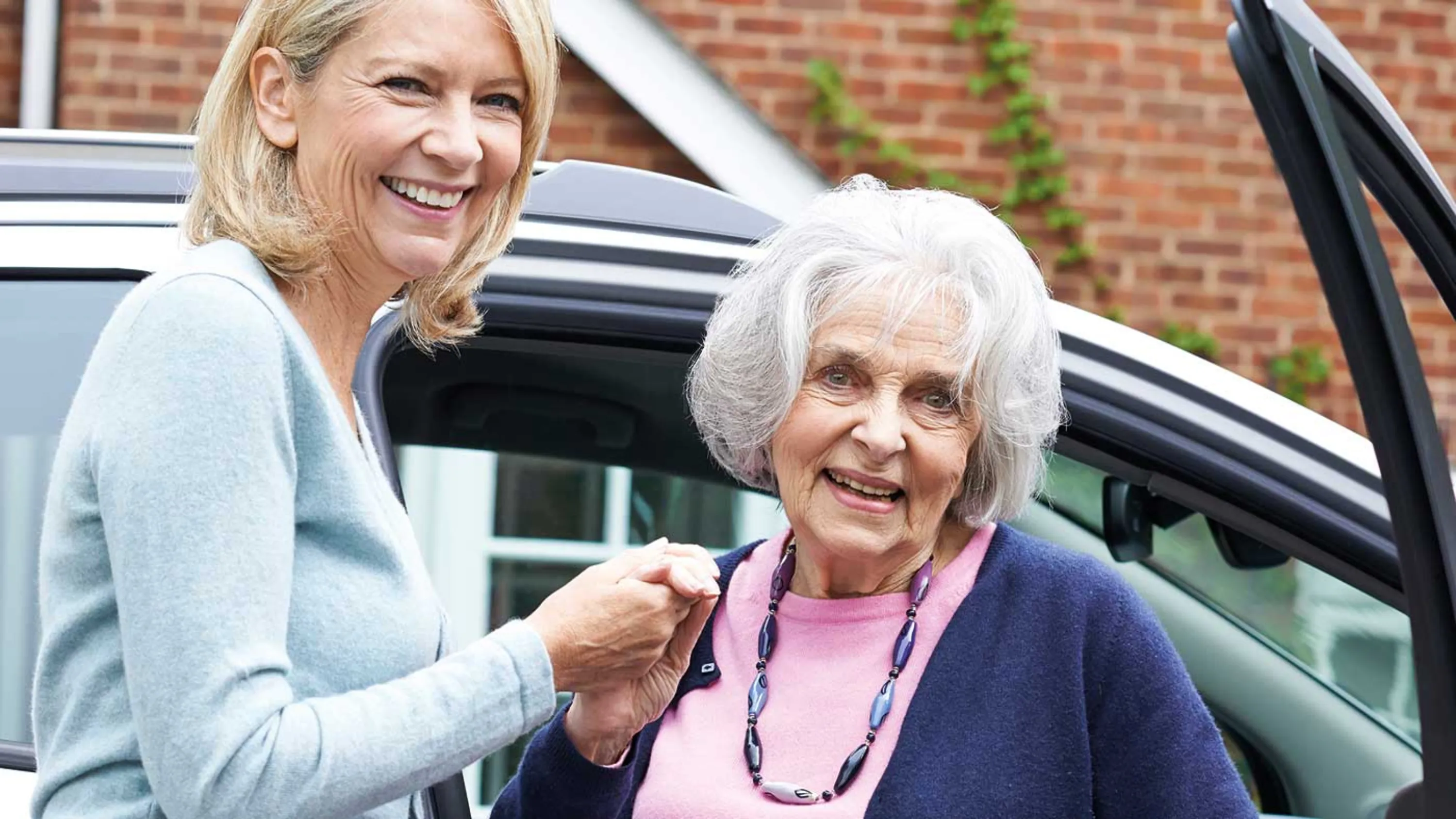 Eine Frau hilft einer Senior aus dem Auto.