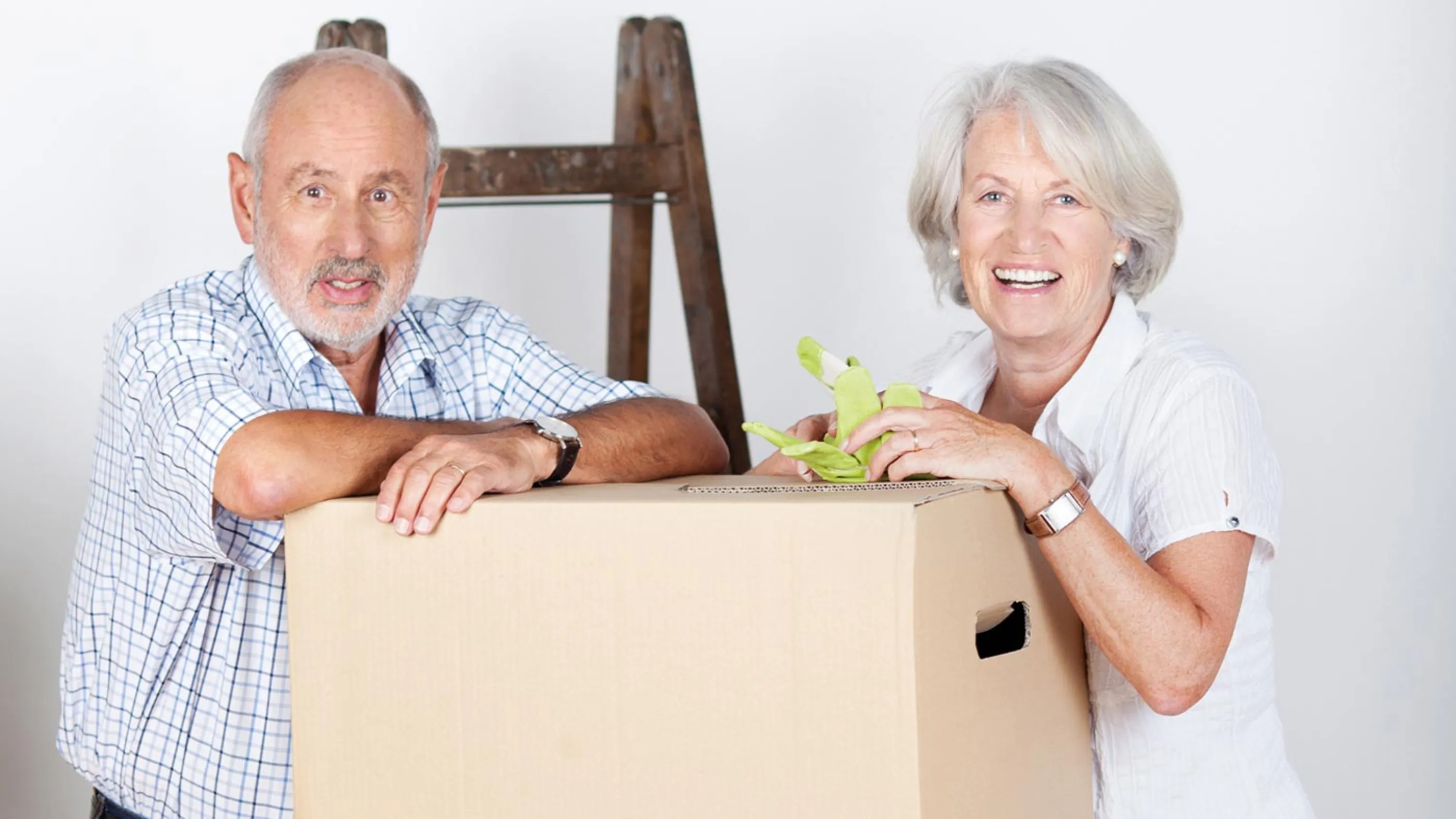 Ein älteres Paar stützt sich auf einem Umzugskarton ab. 