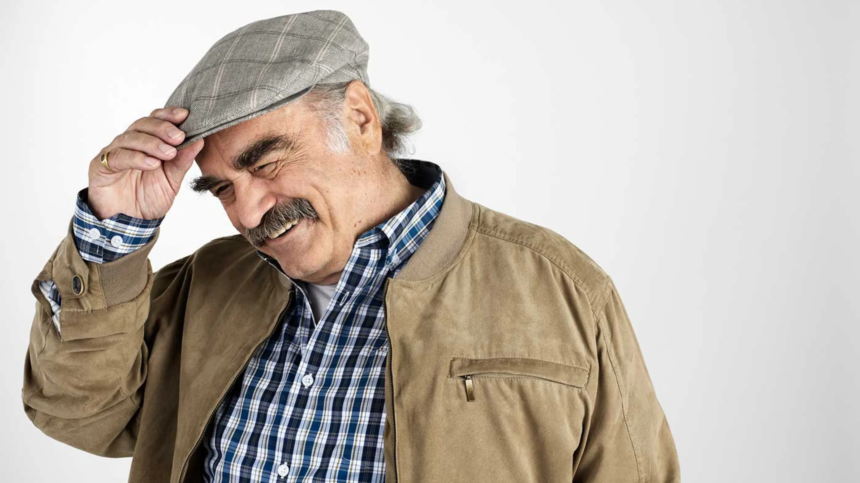 Ein lachender Senior hält sich den Hut. 