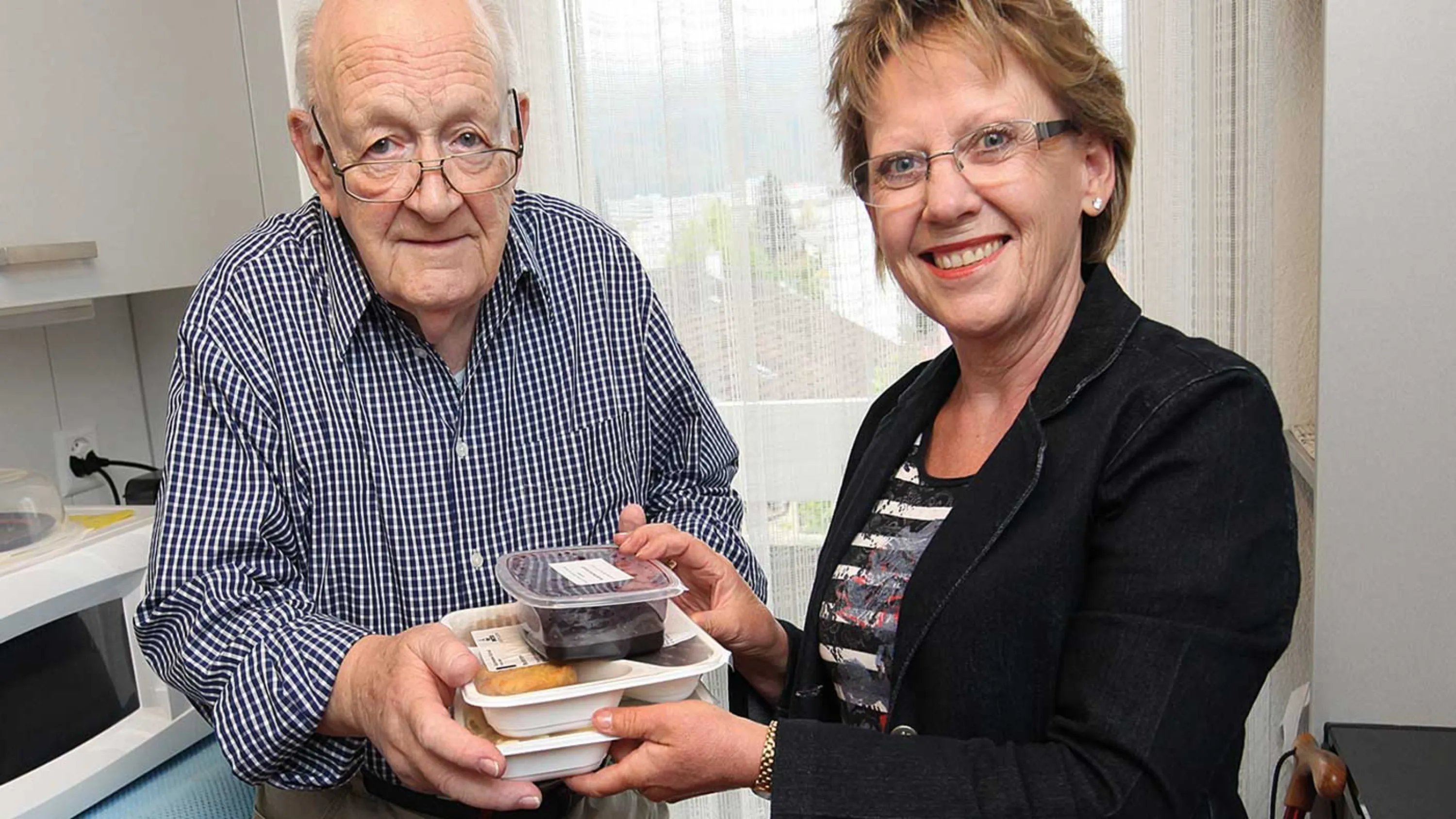 Eine Mahlzeitenverträgerin übergibt einem Senior die Mahlzeiten. 