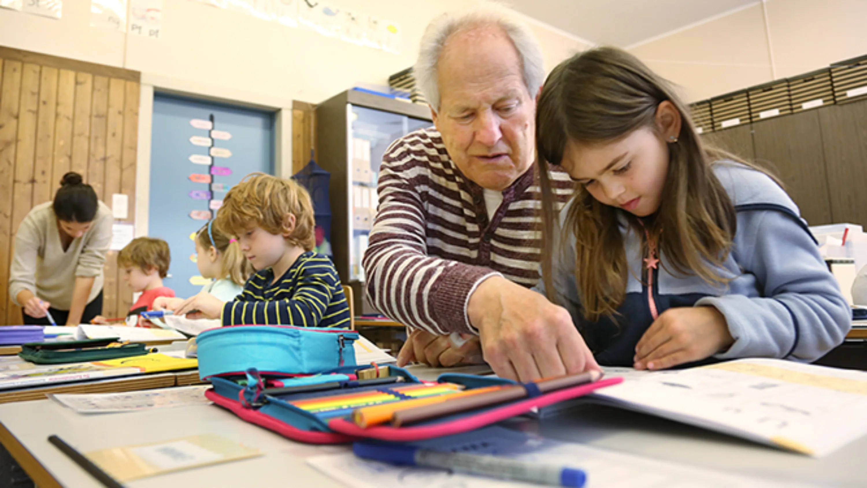 Eine Seniorin musiziert mit einer Klasse vor der Wandtafel.
