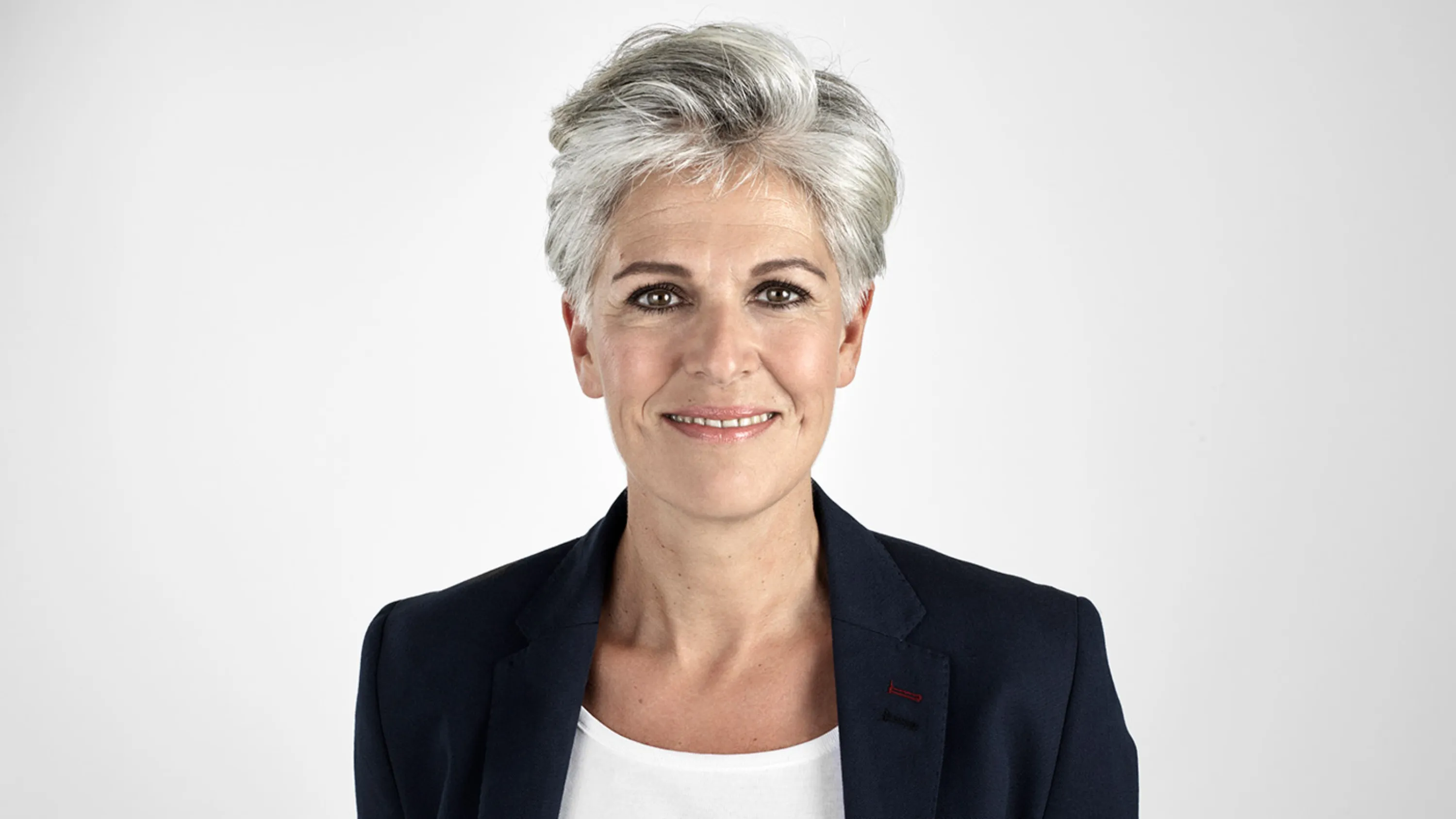 Frau mit grauen Haaren schaut lächelnd in die Kamera