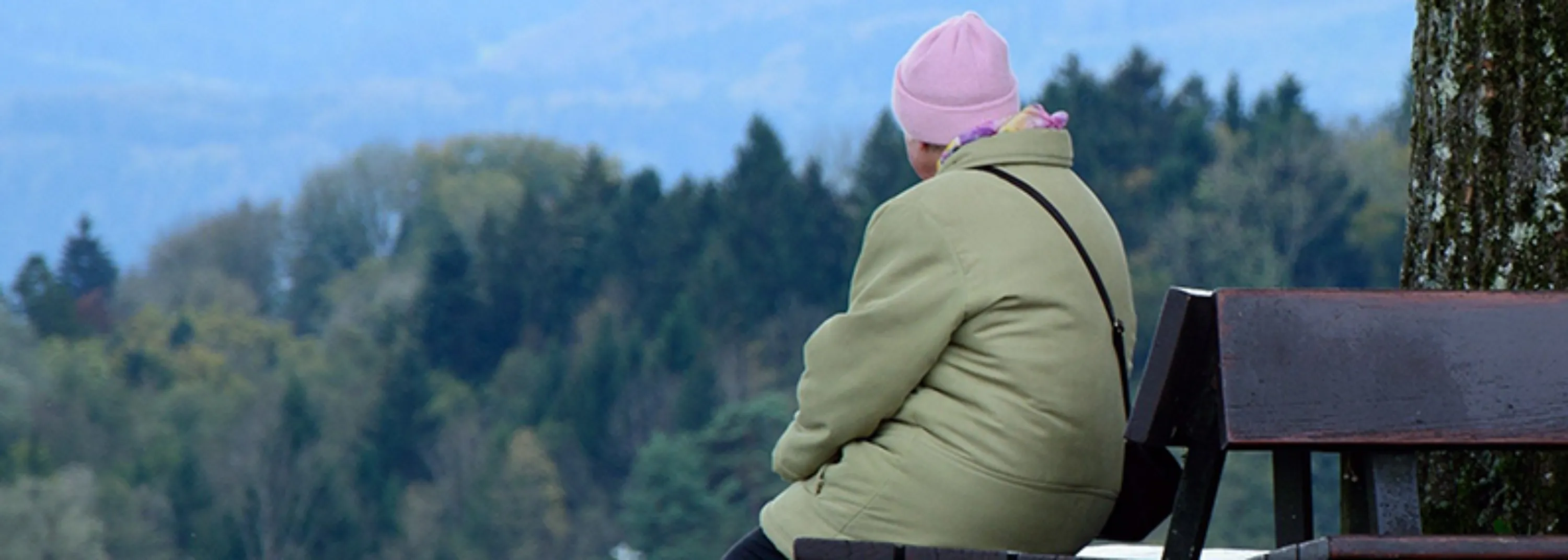 Frau von hinten sitzt auf Bänkli und schaut in die Natur