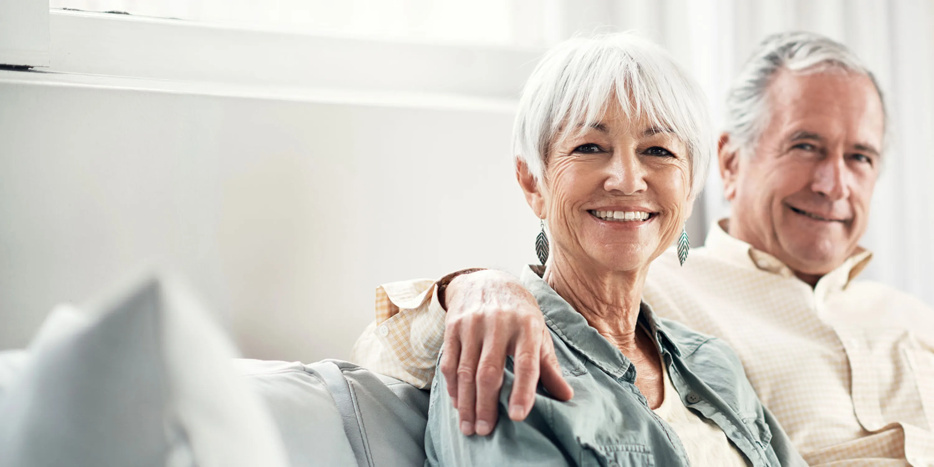 Ein älteres Paar sitzt auf dem Sofa und schaut sehr zufrieden, weil der Steuererklärungsdienst die Steuererklärung kompetent ausgefüllt hat.
