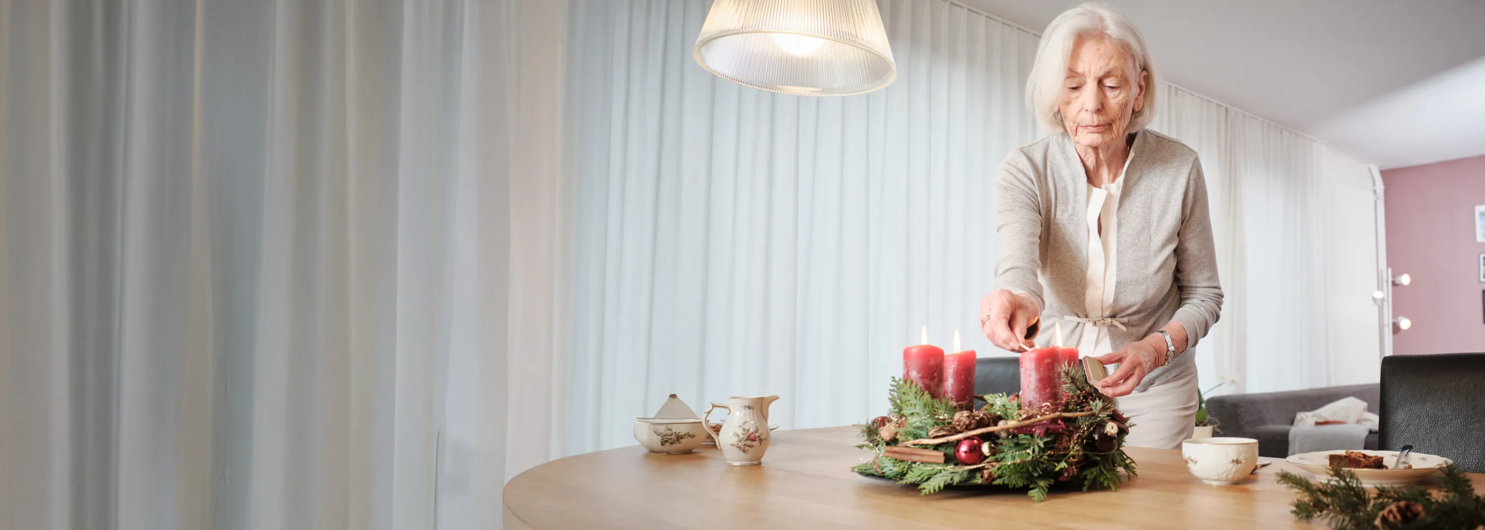 Ältere Dame zündet Kerzen auf Adventskranz an.