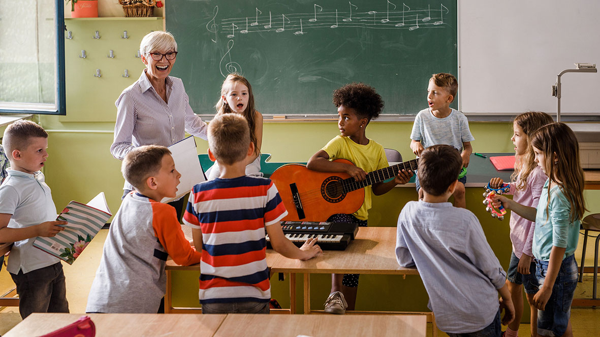 Eine Seniorin musiziert mit einer Klasse vor der Wandtafel.