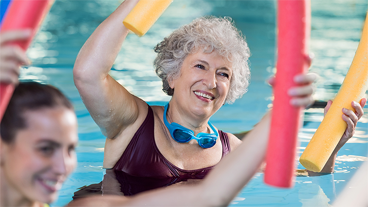 Eine Seniorin liegt beim Wasserfitness auf dem Rücken in Wasser und trainiert ihre Beine.