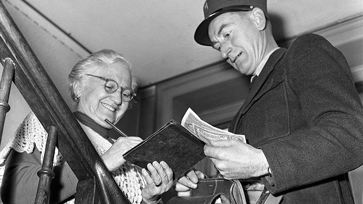 Un facteur verse la prime AVS à une retraitée, en octobre 1955 (image Keystone-ATS/Jules Vogt).